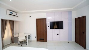 Habitación de hotel con cama, escritorio, silla, televisor montado en la pared y armario.