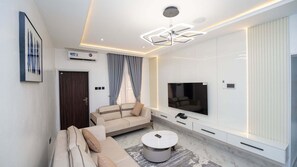 A modern living room with a sofa, coffee table, TV, and built-in cabinets. - Cholis Residency (Abuja)
