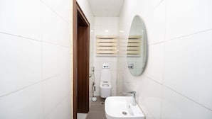 A bathroom with white tiled walls, a wooden door, a white toilet, a bidet, a mirror, and a sink. - Cholis Residency (Abuja)