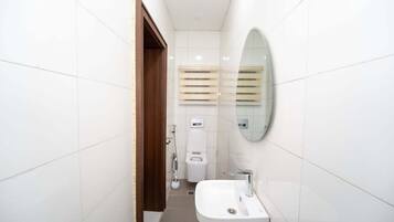 A bathroom with white tiled walls, a wooden door, a white toilet, a bidet, a mirror, and a sink.