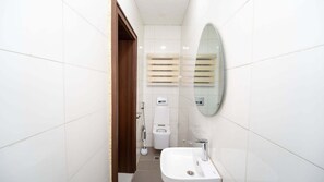 Un baño con paredes de azulejos blancos, una puerta de madera, un inodoro blanco, un bidé, un espejo y un lavamanos.