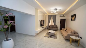 A modern living room with a flat-screen TV, a sofa, a coffee table, and a potted plant. - Cholis Residency (Abuja)