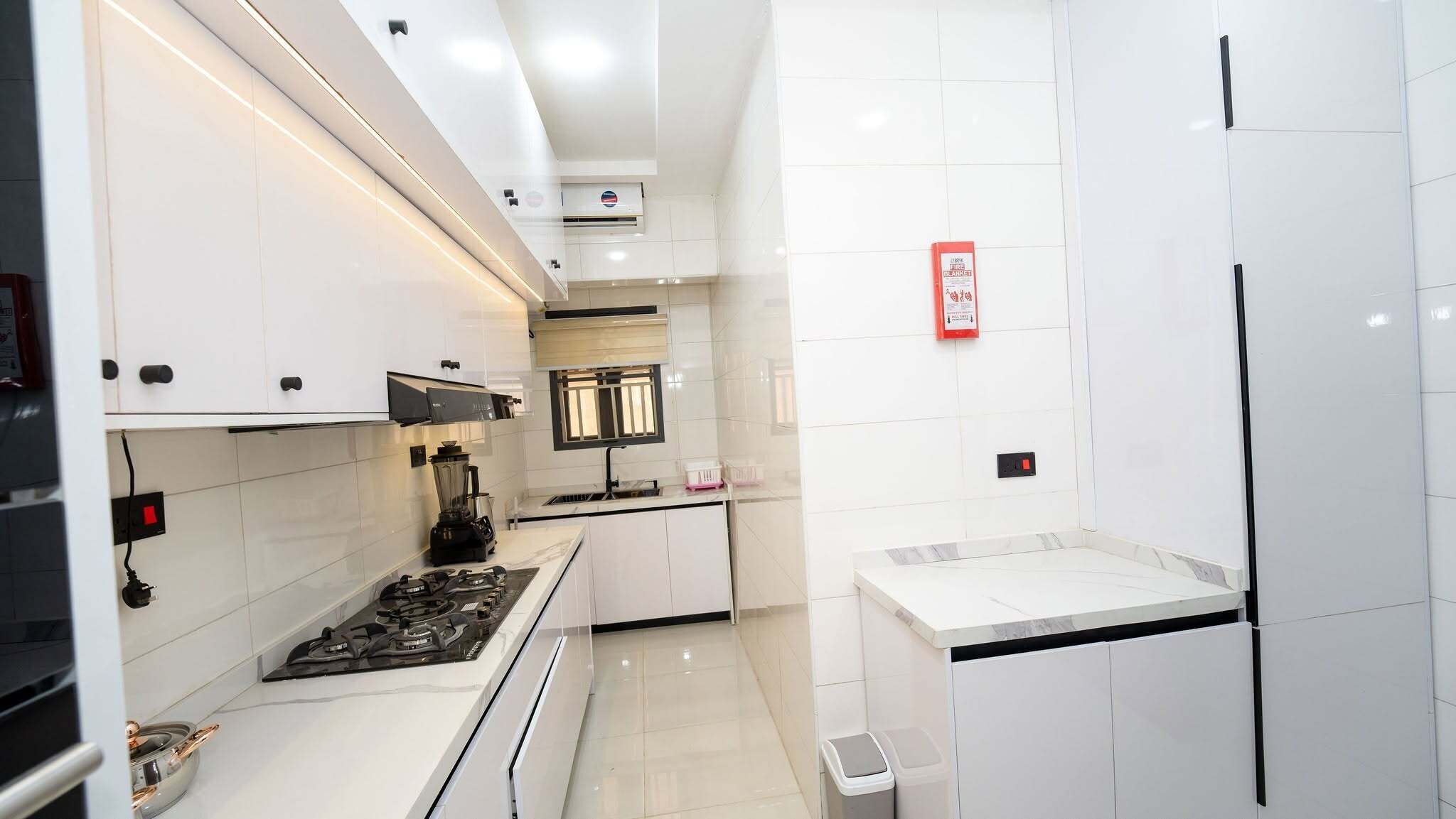 A modern kitchen with white cabinets, a gas stove, a blender, and a fire blanket.
