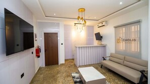 A modern living room with a flat-screen TV, a sofa, a coffee table, a fireplace, and a wall-mounted air conditioning unit. - Cholis Residency (Abuja)