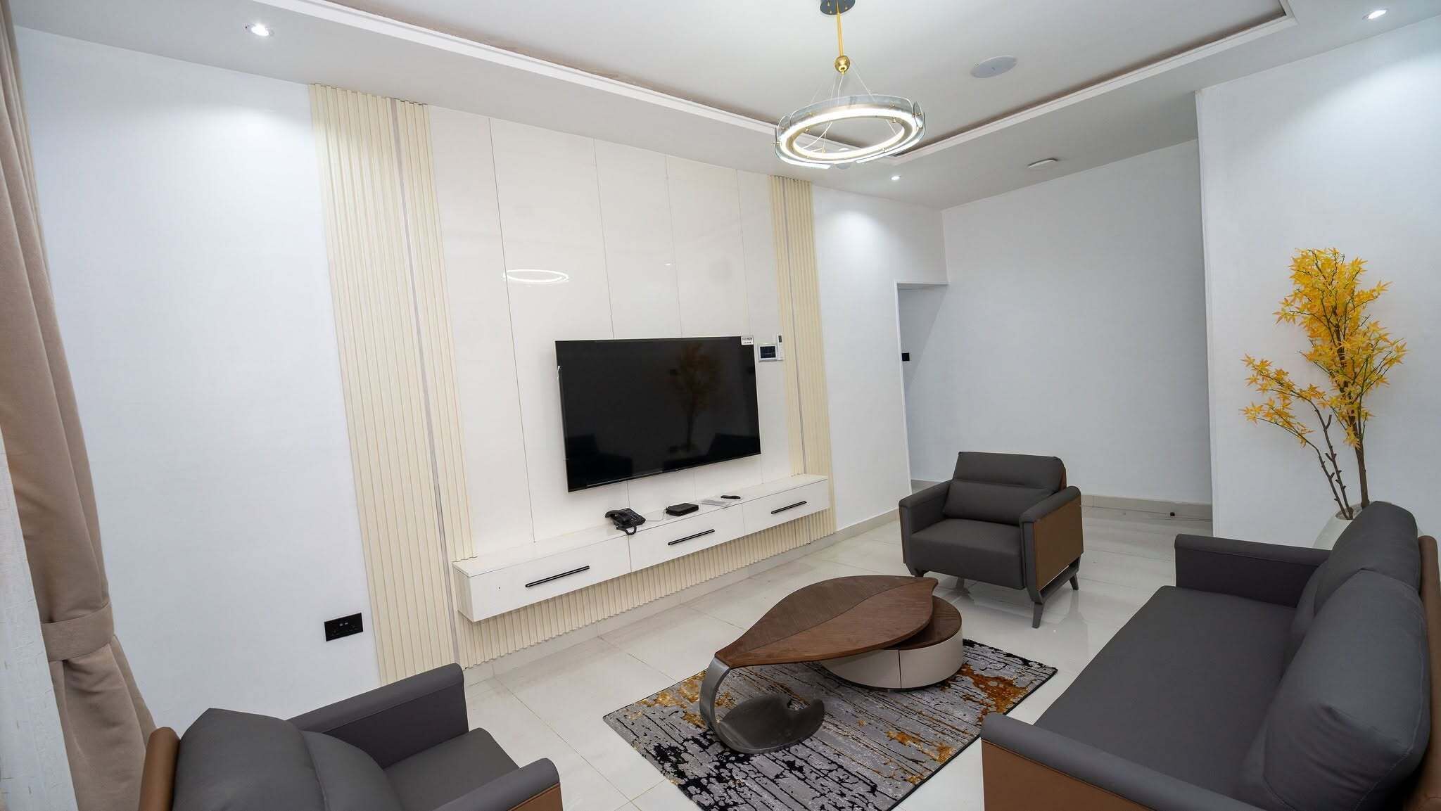 A modern living room with a flat-screen TV, two sofas, a coffee table, and a decorative plant.