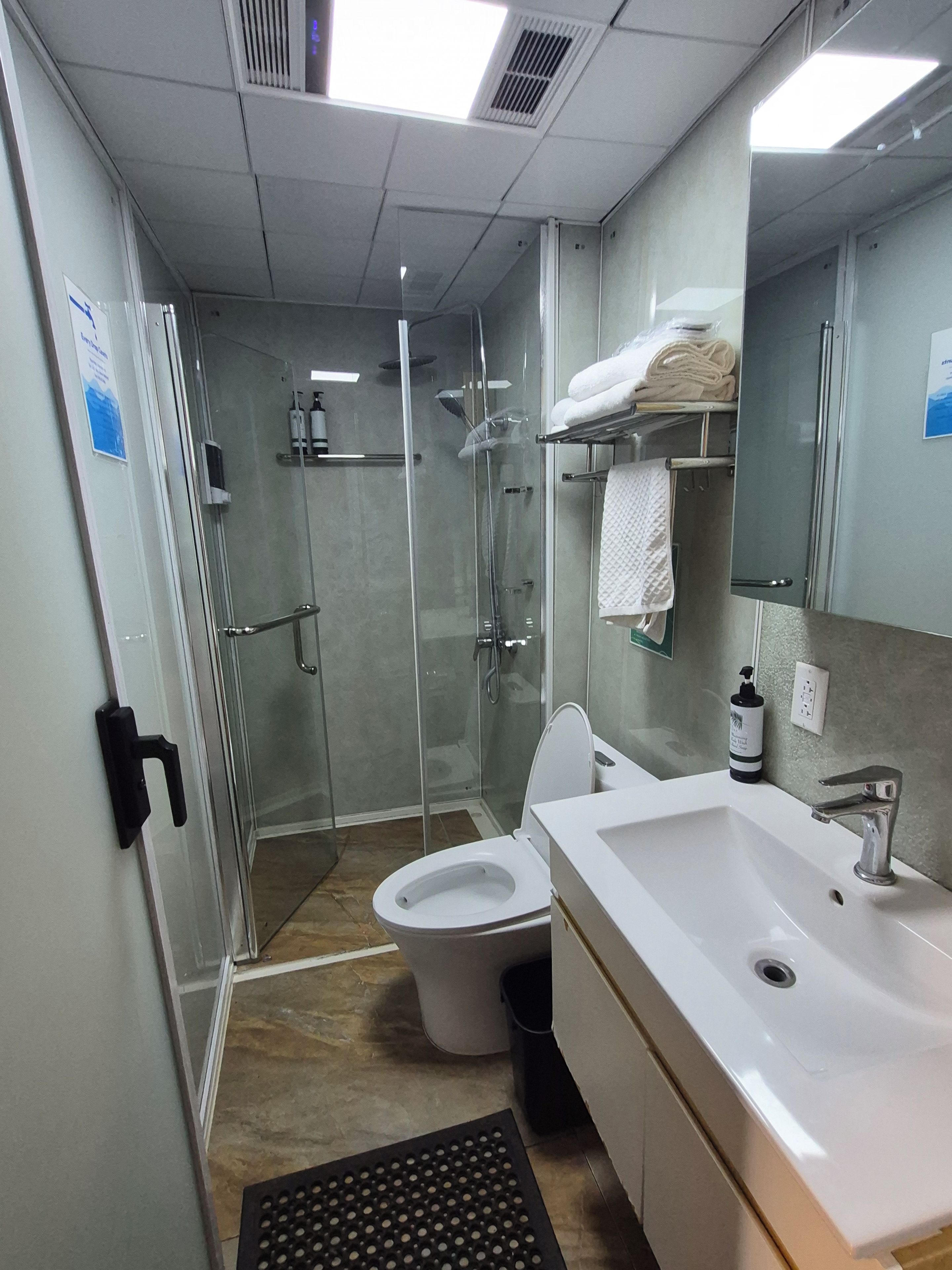 Un baño moderno con ducha acristalada, inodoro, lavabo con espejo y perchero para toallas.