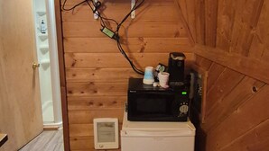 Una habitación pequeña con paredes de madera, un refrigerador blanco, un microondas, un televisor montado en la pared y una puerta que da a otra habitación.