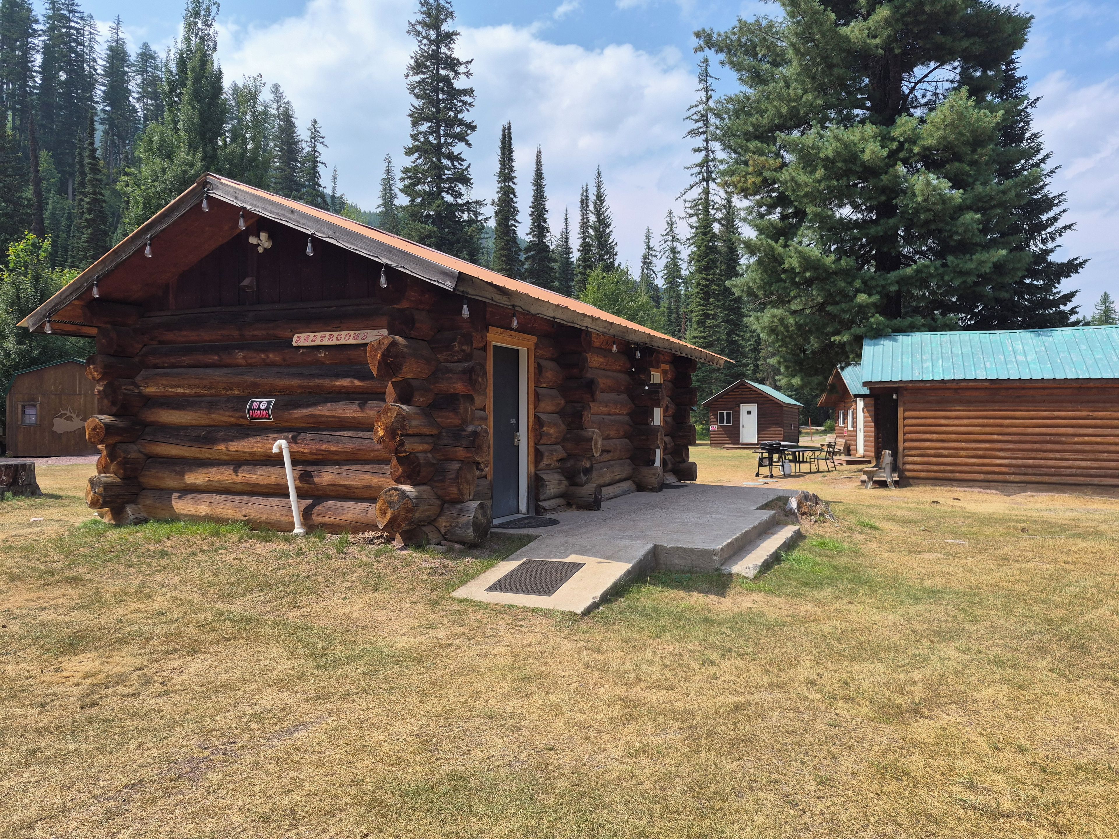 A rustic log cabin with a door, a sign indicating 'No Parking,' and a small outdoor seating area.