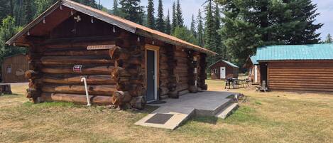 A rustic log cabin with a door, a sign indicating 'No Parking,' and a small outdoor seating area.
