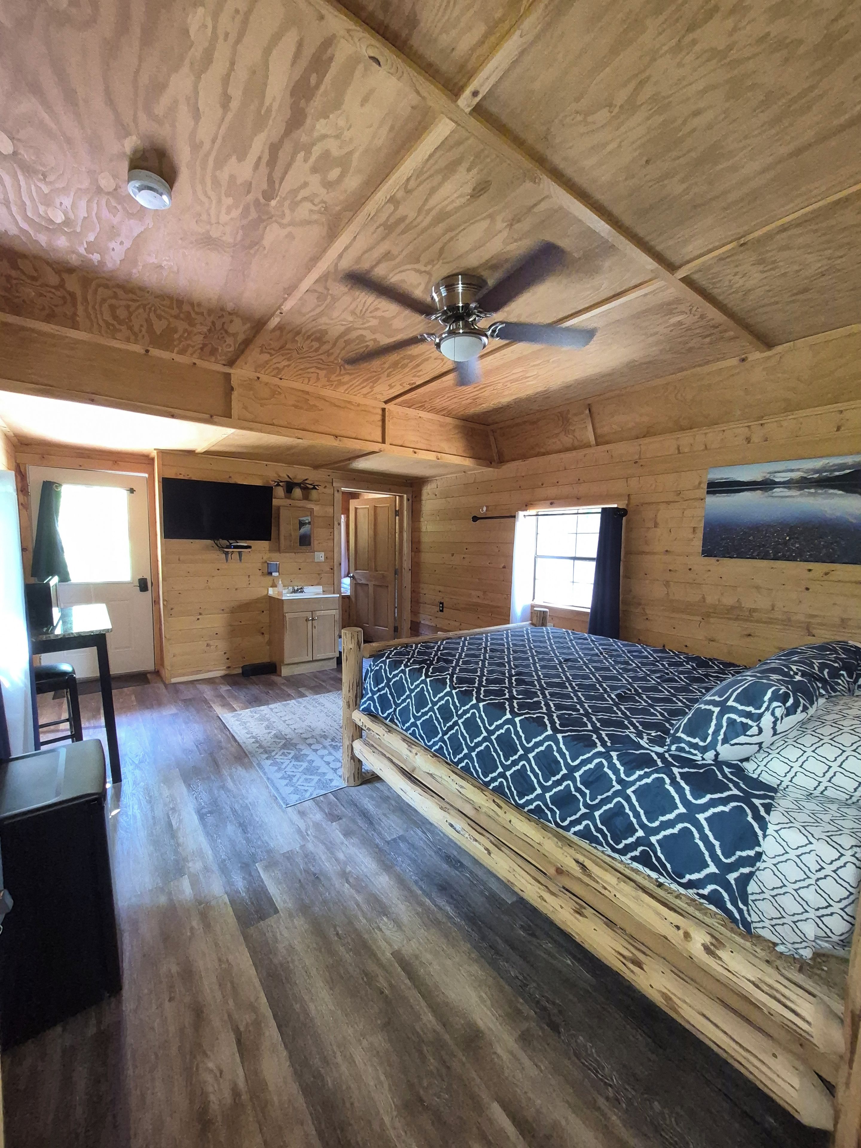 L’intérieur d’une cabane en bois, avec un lit, un bureau et un ventilateur de plafond.