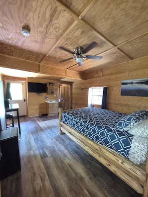 A wooden cabin interior with a bed, desk, and ceiling fan. - Aurora Resort (Essex)