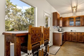 A kitchen with wooden cabinets, a built-in stove, and a window overlooking trees. - Cliffside Lodge + Hill Country Views (Wimberley)