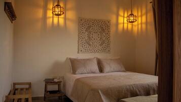 Um quarto com cama, duas mesas de cabeceira, um objeto decorativo na parede e dois lustres.