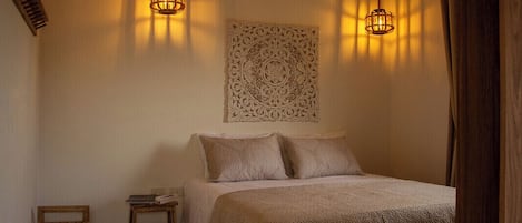 A bedroom with a bed, two bedside tables, a decorative wall piece, and two hanging light fixtures.