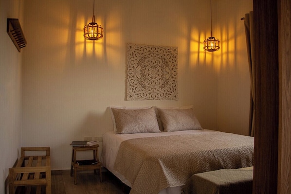 A bedroom with a bed, two bedside tables, a decorative wall piece, and two hanging light fixtures.