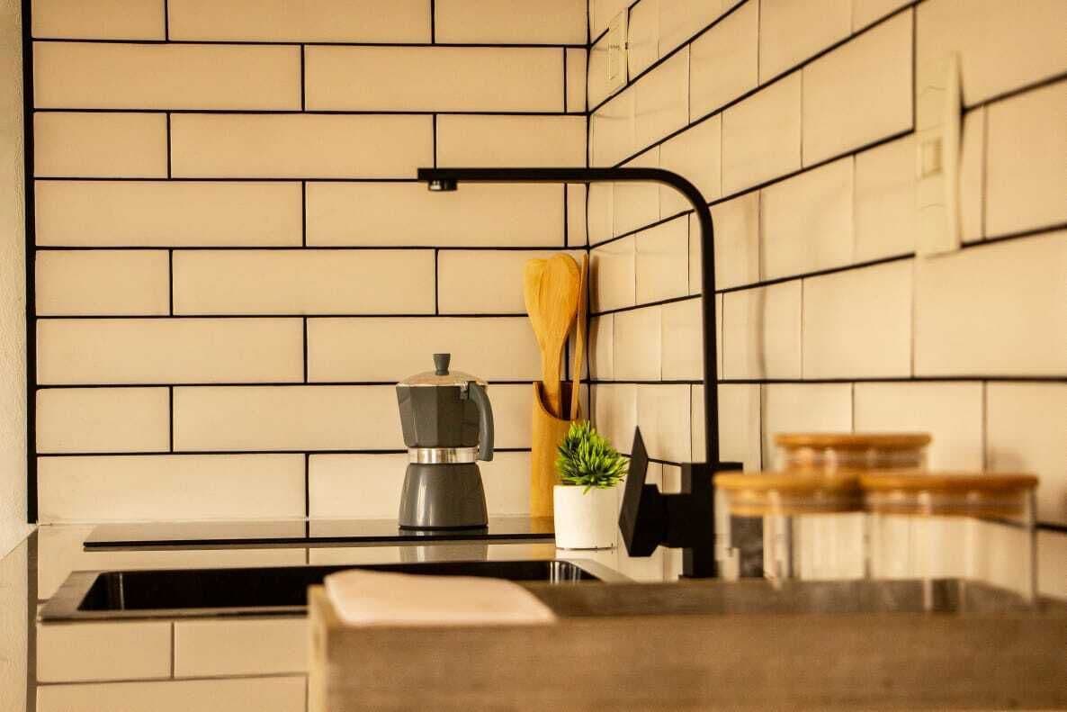 Una cocina con salpicadero de ladrillo, una cafetera sobre la encimera, una cuchara de madera y una planta en maceta.