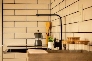A kitchen with a brick backsplash, a coffee maker on the counter, a wooden spoon, and a potted plant.