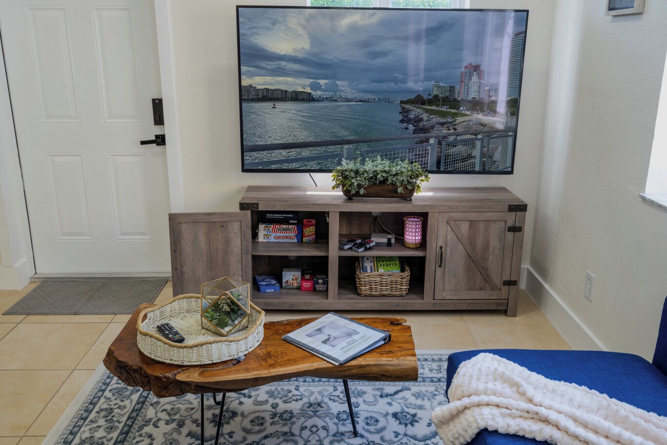 A living room with a television mounted on the wall, a wooden coffee table with a basket and a book, a blue sofa, and a cabinet with books and decorative items.
