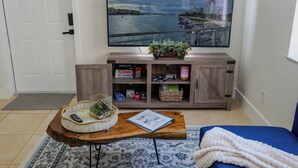 Een woonkamer met een aan de muur bevestigde televisie, een houten salontafel met een mand en een boek, een blauwe bank en een kast met boeken en decoratieve objecten.