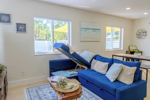 Una sala de estar con un sofá azul, un sillón reclinable, una mesa de centro y vistas al exterior a través de amplios ventanales.