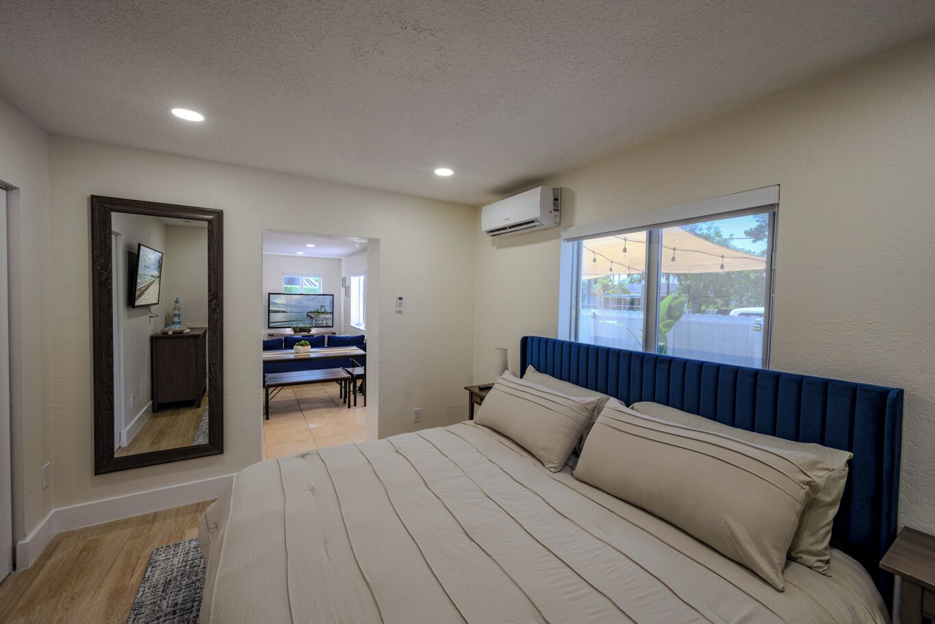 A bedroom with a large bed, a window, an air conditioning unit, and a view of the outside.