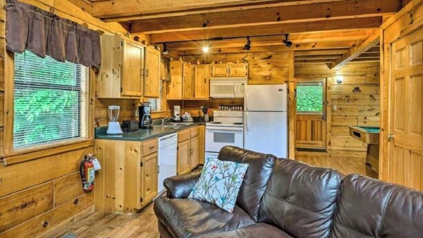 A cabin interior with a kitchenette, a leather sofa, wooden walls, and a window with blinds. - Best Location - Walk to Town - Hot Tub - Fireplace (Gatlinburg)