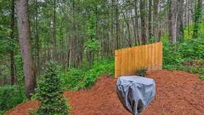 A wooded area with a wooden fence and a covered object, possibly a grill, on a pile of mulch. - Best Location - Walk to Town - Hot Tub - Fireplace (Gatlinburg)
