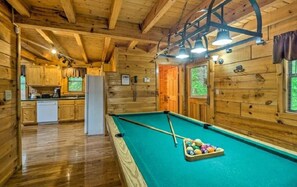 Ein Holzblockhaus-Innenraum mit Billardtisch, Küchenzeile und Holzwänden.