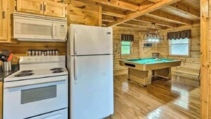A wooden cabin interior with a kitchen area including a stove, microwave, refrigerator, and a pool table. - Best Location - Walk to Town - Hot Tub - Fireplace (Gatlinburg)