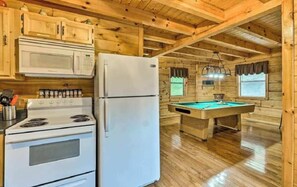 Ein Holzblockhaus-Innenraum mit Küchenzeile, inklusive Herd, Mikrowelle, Kühlschrank und Billardtisch.
