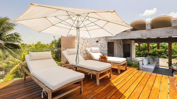 A wooden deck with lounge chairs and a large umbrella, surrounded by greenery and a stone wall. - Villa Romeo | Jungle & Caribbean • Rooftop Pool (Tulum)
