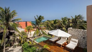 A rooftop pool with lounge chairs and an umbrella, surrounded by palm trees and a view of the ocean. - Villa Romeo | Jungle & Caribbean • Rooftop Pool (Tulum)