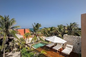 A rooftop pool with lounge chairs and an umbrella, surrounded by palm trees and a view of the ocean. - Villa Romeo | Jungle & Caribbean • Rooftop Pool (Tulum)