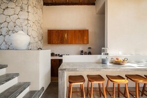 A kitchen with a stone wall, wooden cabinets, a marble countertop, and wooden stools. - Villa Romeo | Jungle & Caribbean • Rooftop Pool (Tulum)