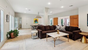 Uma sala de estar espaçosa com um conjunto de sofá marrom, uma mesa de centro e um espaço de jantar com mesa e cadeiras.