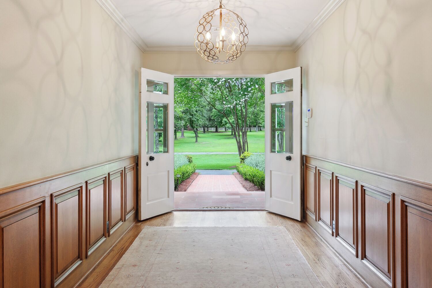 A hallway with a wooden floor, white walls, and a door leading to a garden.