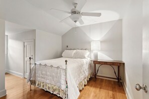 Ein Schlafzimmer mit einem Bett, einem Nachttisch, einem Deckenventilator und einer Tür.