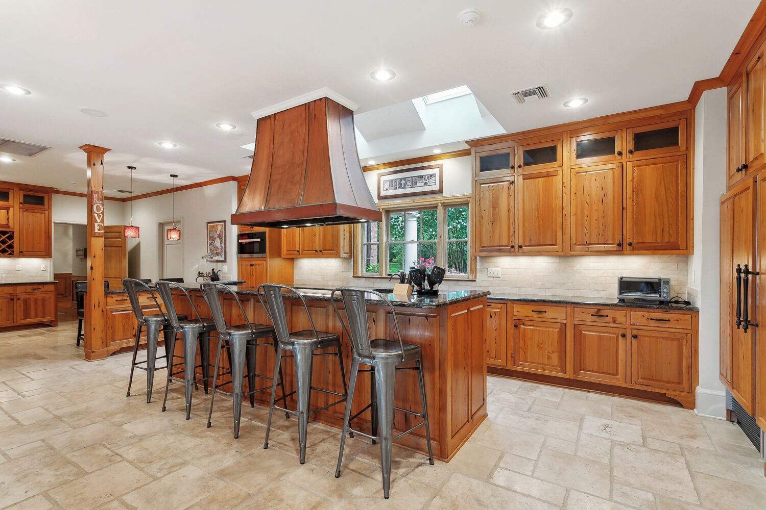 A modern kitchen with wooden cabinets, a central island with bar stools, and a skylight.