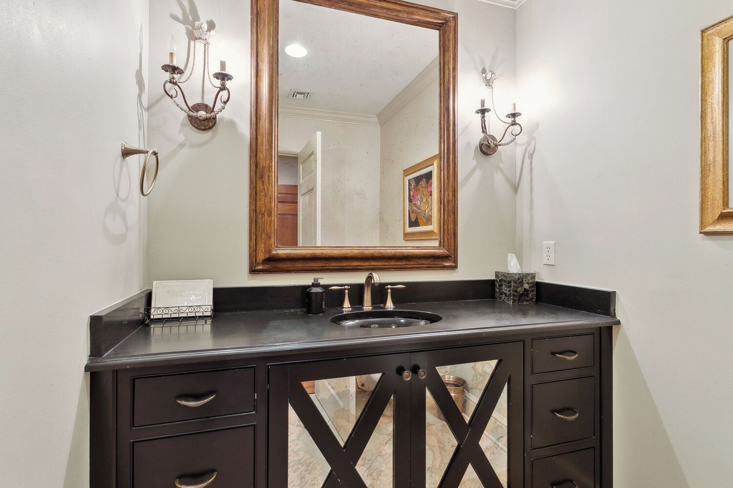 A bathroom with a dark vanity, a mirror, a sink, and two wall-mounted sconces.