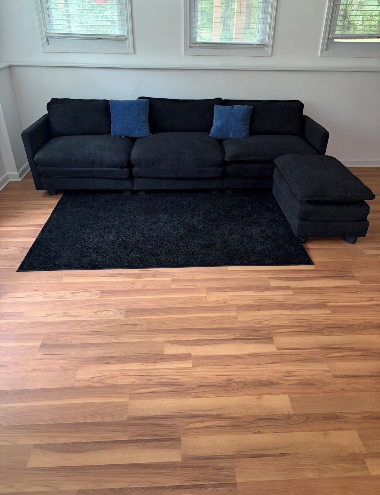 Ein modulares Sofa mit dunklem Teppich in einem Raum mit Holzboden und Fenstern.