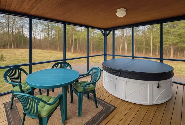A covered deck with a hot tub, a round table, and four chairs.
