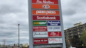Un letrero vertical con varios nombres de comercios, incluyendo Food Basics, Shoppers Drug Mart y Tim Hortons.