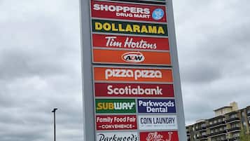 Un letrero vertical con varios nombres de comercios, incluyendo Food Basics, Shoppers Drug Mart y Tim Hortons.