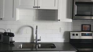 Una cocina con gabinetes blancos, un lavamanos de acero inoxidable, un microondas y un horno.