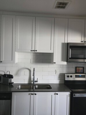 Una cocina con gabinetes blancos, un lavamanos de acero inoxidable, un microondas y un horno.
