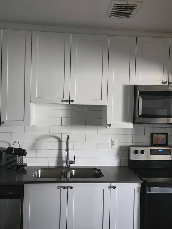 A kitchen with white cabinets, a stainless steel sink, a microwave, and an oven.