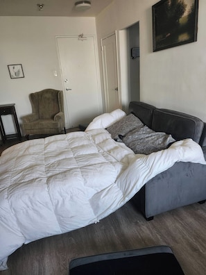 A bedroom with a large bed, a chair, a door, and a painting on the wall. - 1 bd Apartment Sleeps 4- 20 Mins From Everything! (Toronto)