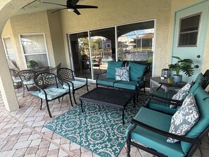 A covered patio area with outdoor furniture, a ceiling fan, and a view through large glass doors. - Sun-Soaked SW Cape Coral Gulf Access Retreat (Cape Coral)