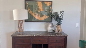 A dark wood cabinet with drawers and a wine rack, a framed map on the wall, a lamp, and a potted plant. - Sun-Soaked SW Cape Coral Gulf Access Retreat (Cape Coral)