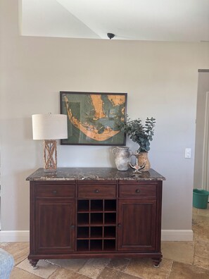 A dark wood cabinet with drawers and a wine rack, a framed map on the wall, a lamp, and a potted plant. - Sun-Soaked SW Cape Coral Gulf Access Retreat (Cape Coral)